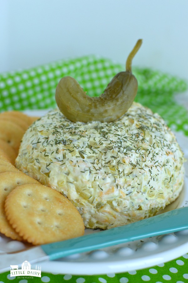 a cheese ball has a pickle sitting on the top with round butter crackers surrounding it. 