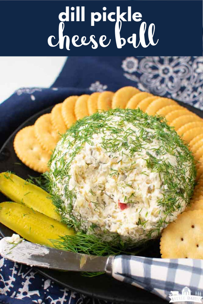 a cheese ball that's has a portion of it removed to show the inside of the cheese ball. On a black plate with round crackers and pickle slices