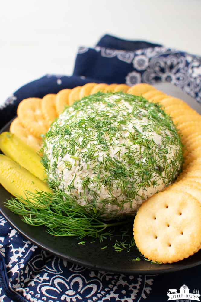 a cheeseball sprinkled with minced fresh dill weed, surrounded by butter crackers and pickle slices